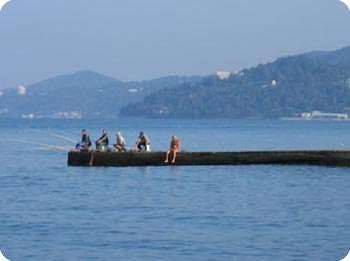 Fuenf Angler sitzen auf Steg am Meer